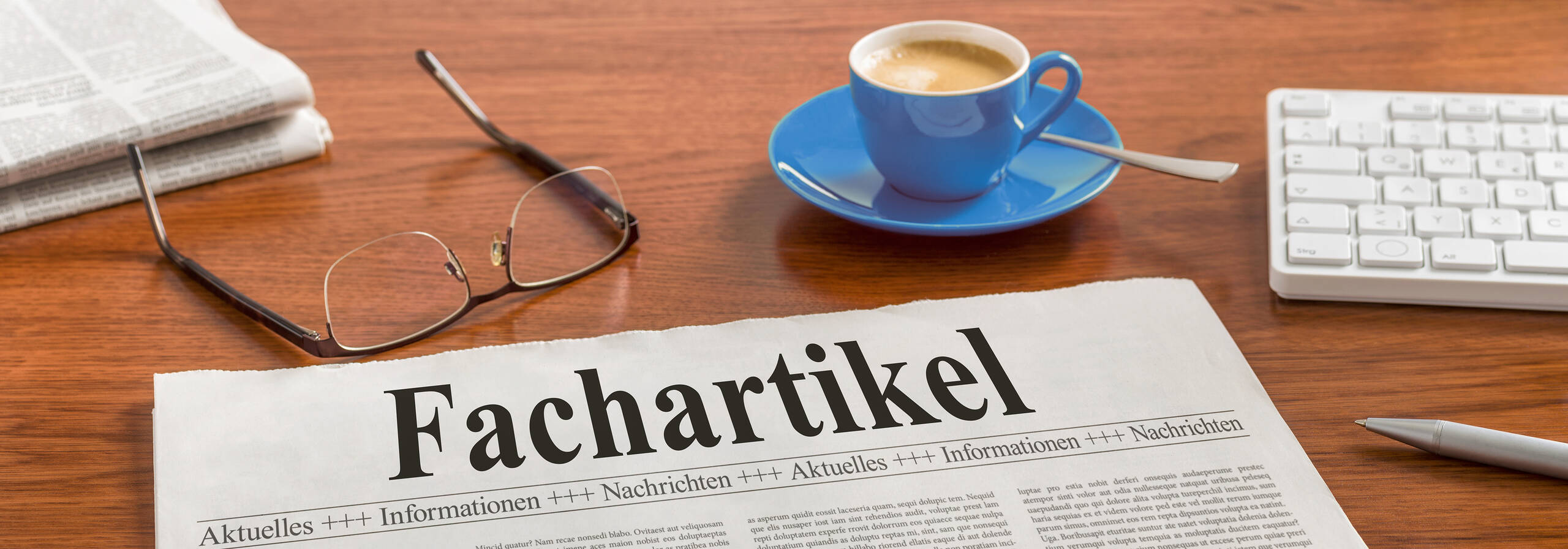 Fachartikel Zeitung, Brille, Tastatur und Tasse auf Tisch